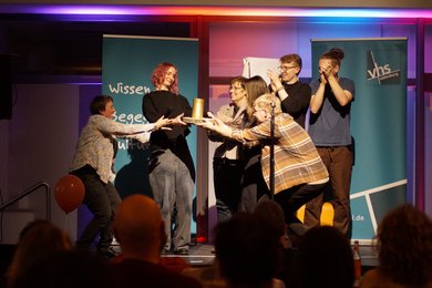 Annika Blanke und die Slam Poeten übergeben Siegerin Monika Mertens die goldende Grünkohldose als Gewinn.