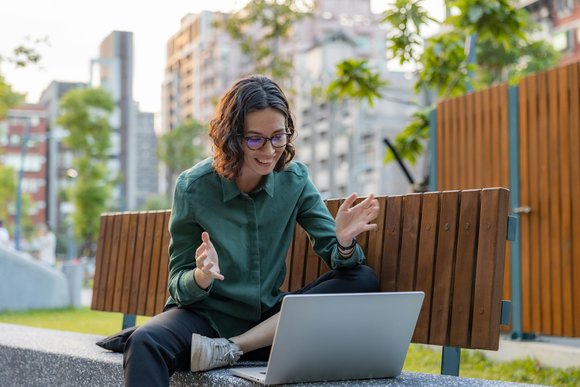 Eine Frau sitzt auf einer Parkbank und schaut auf einen Laptop