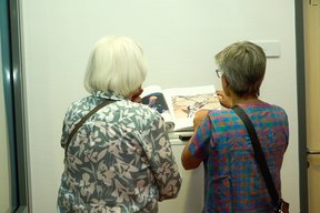 Bild: VHS Oldenburg Zwei Gäste schauen sich das Buch zur Ausstellung an