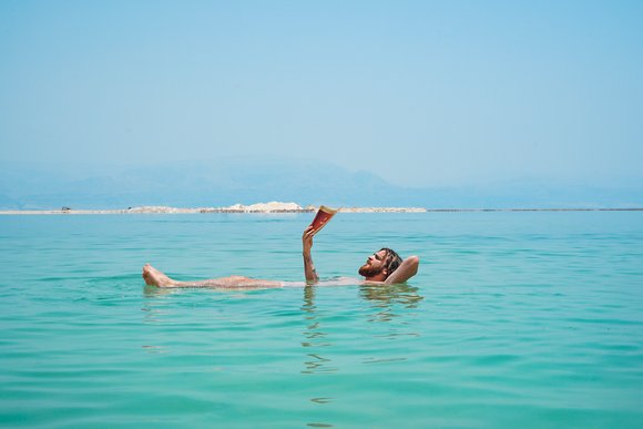 Ein Mann treibt auf dem Rücken liegend auf dem Meer und liest ein Buch.