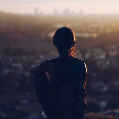 Eine Frau sitzt auf einem Hügel und schaut auf eine Stadt herunter.