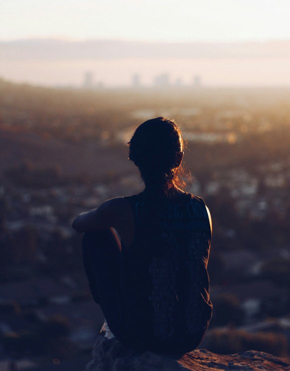 Eine Frau sitzt auf einem Hügel und schaut auf eine Stadt herunter.