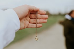 Eine Hand hält eine Kette mit einem David-Stern als Anhänger.