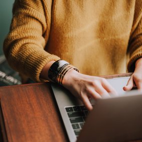 Ein person in einem gelben Pullover bedient einen Laptop.